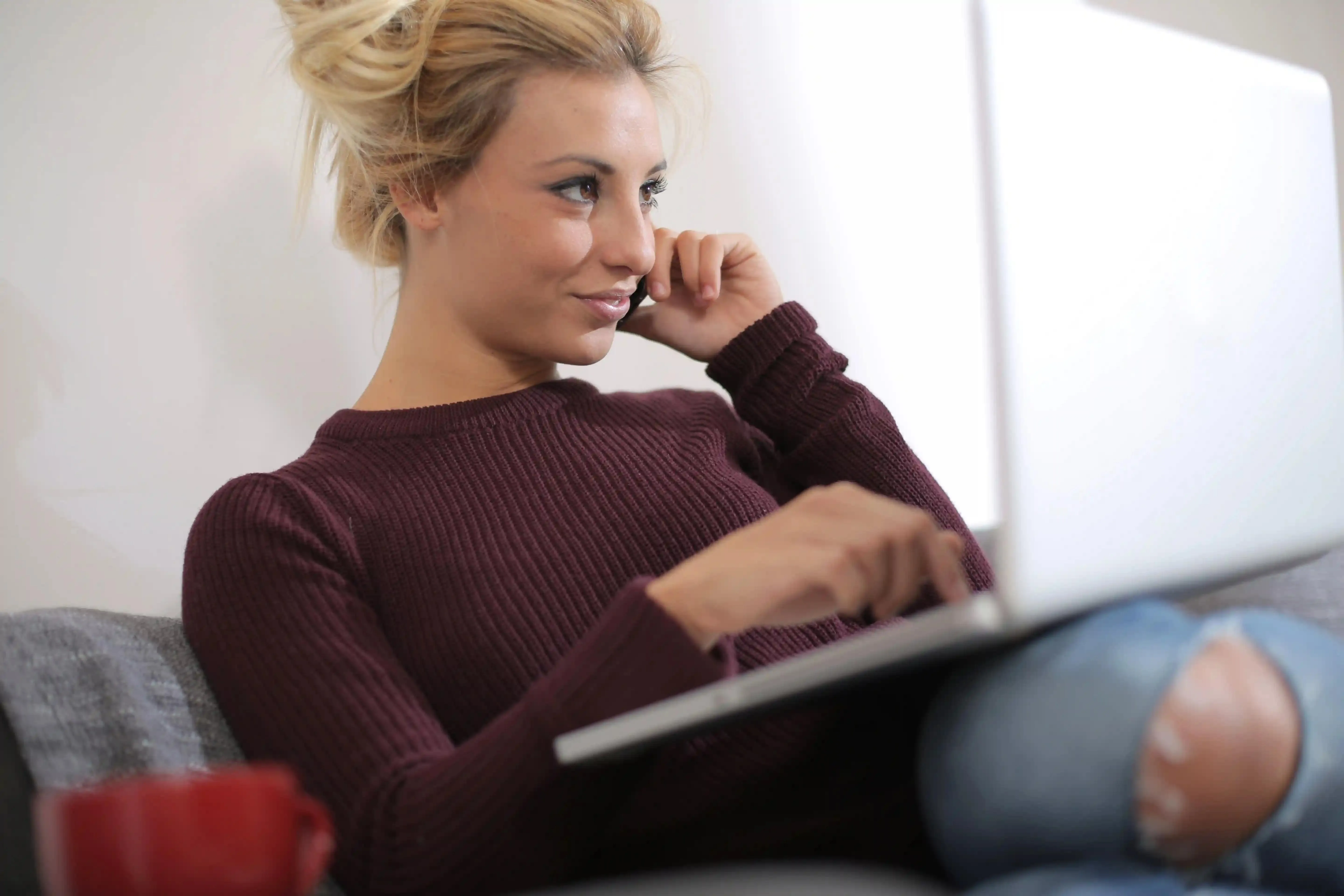 žena sedí s laptopem na klíně a telefonuje