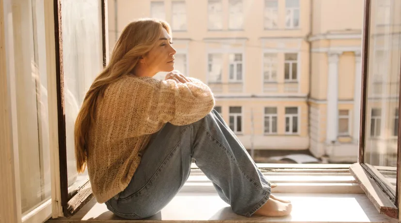 mladá žena sedí na parapetu, je zamyšlená a dívá se mimo