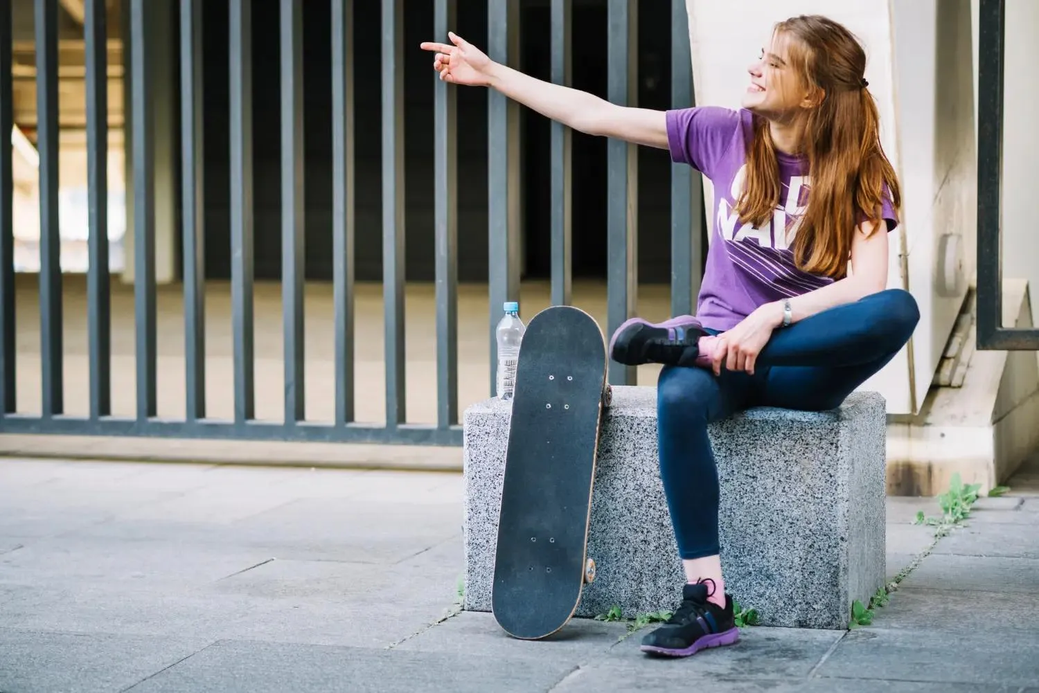 dívka sedí na betonu a vedle sebe má skateboard