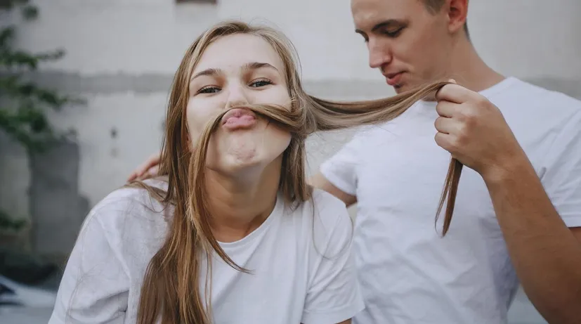 dívka s chlapcem venku, ona si z vlasů dělá knír