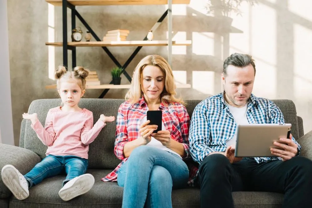 rodiče jsou na mobilu a tabletu a dcera sedí sama