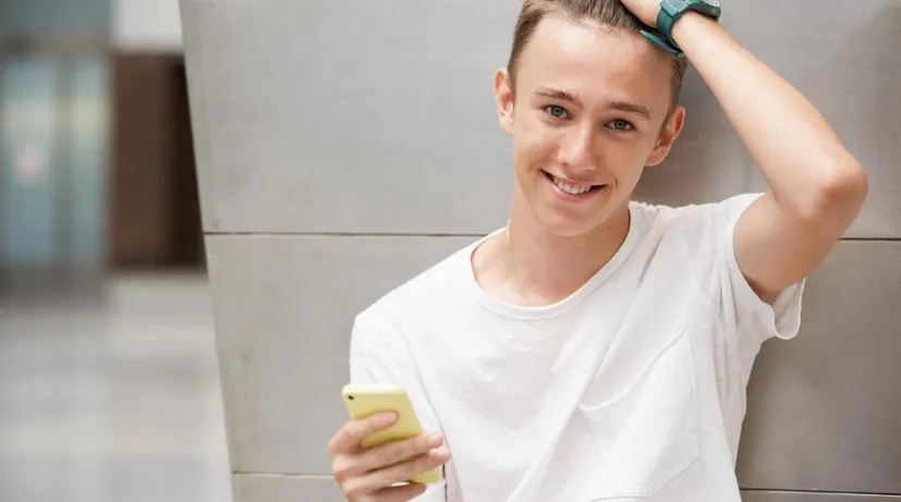 chlapec s mobilem opřený o stěnu
