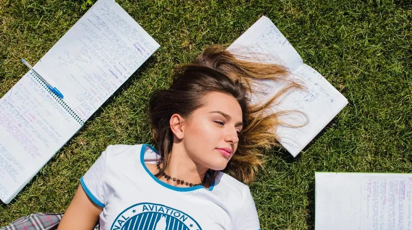 mladá žena leží v trávě a kolem má poznámky do školy