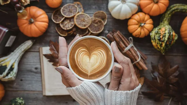 žena drží latté v ruce, za ní podzimní věci jako dekorace