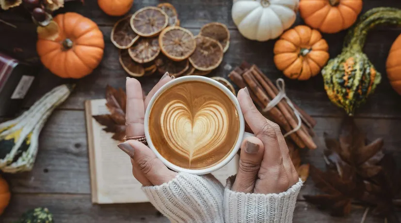 žena drží latté v ruce, za ní podzimní věci jako dekorace