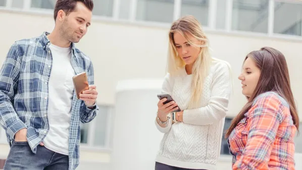 Tři mladí lidé stojí venku a čtou zprávy v mobilech