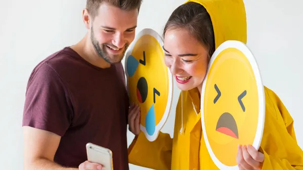 Usměvavá dvojice s mobilem a velkými cedulemi smutných emoji.